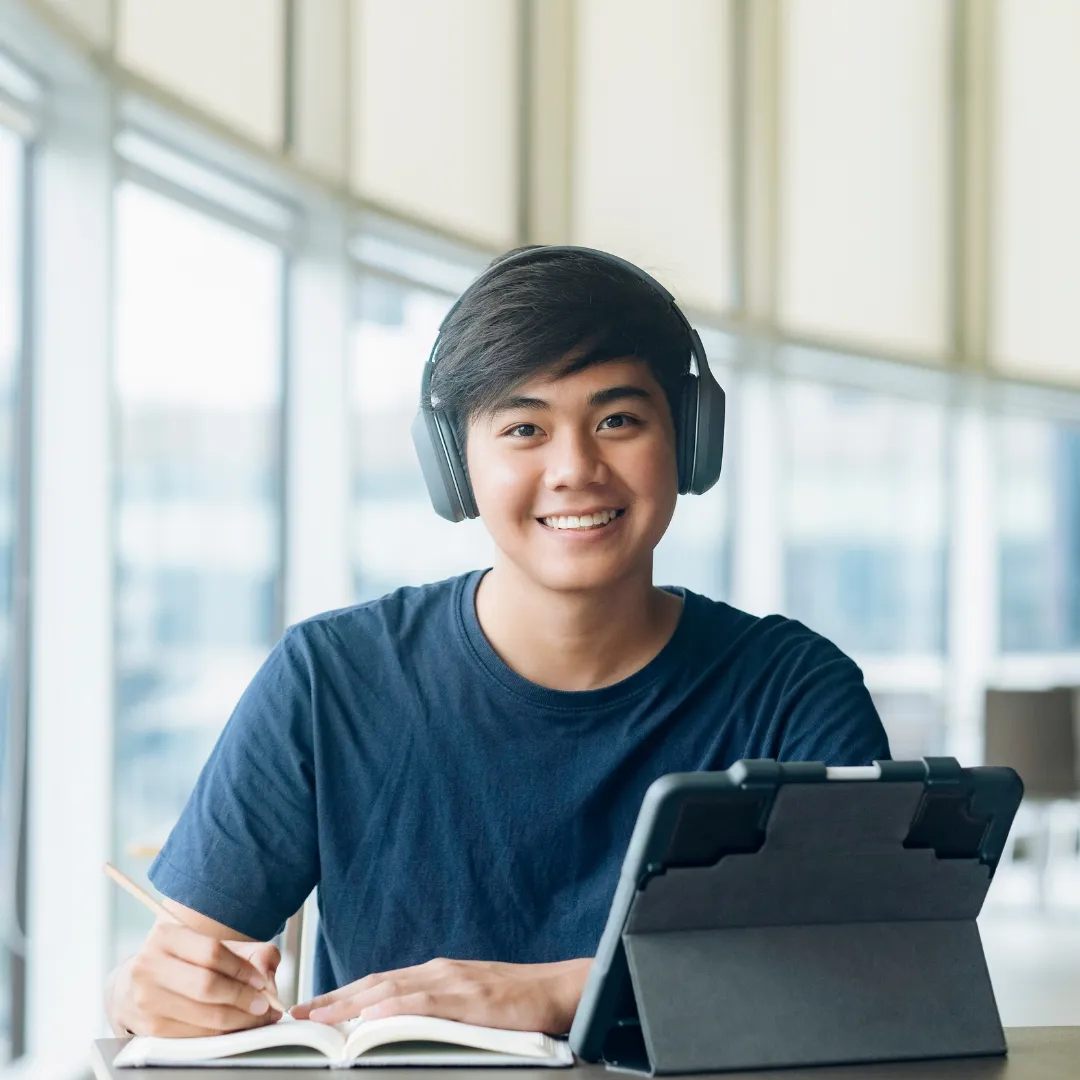 Person wearing headphones sits at a table and large windows in the background.